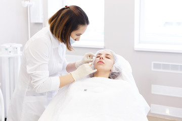 Obraz na płótnie Canvas Hardware and Injections cosmetology. Process of facial beauty injections, biorevitalization of female face procedure in a beauty clinic . Cosmetologist works with patient in a white cosmetology office