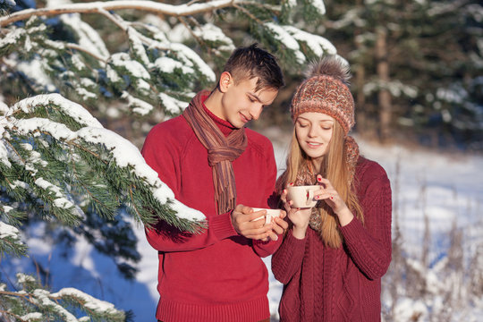 Young couple in love walking in the winter park. Happy couple holding a hot tea  in winter wood