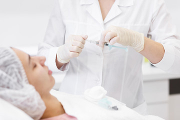 Cosmetology. Preparation in procedure Biorevitalization of the face procedure in a beauty parlour spa clinic. Doctor opens a syringe at the patient.Hands in gloves holding syringe near patient face