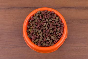 Dry cat food in bowl on wooden background. Pet food on wood surface. Top view