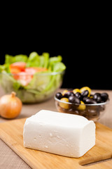 Close up of feta cheese on wooden board on a table ready for serving over black background