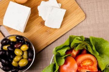 Top view of white cheese on wooden board on a table whith olives, summer salad and cut onions