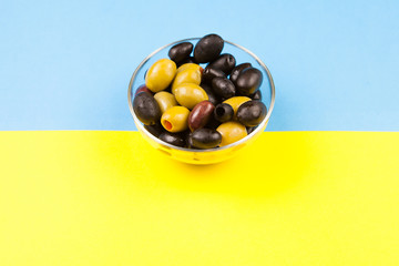 Glass bowl with fresh delicious olives over two colored background in yellow and blue