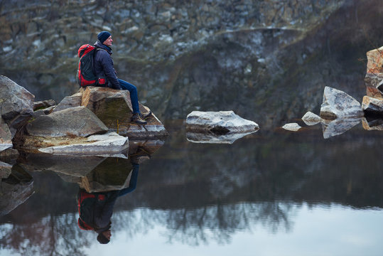 Traveler with a backpack sits on granite stones amidst a calm lake