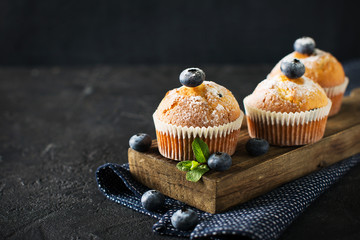 Blueberries muffins or cupcakes with mint leaves on black texture