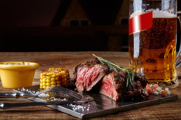 Grilled tenderloin Steak roastbeef and mushrooms sauce on black cutting board and glass of beer on...