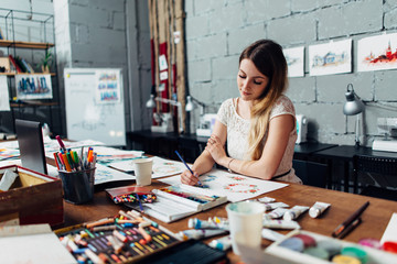 Fototapeta premium Focused young female artist drawing sketches using colored pencils sitting at her stylish workshop