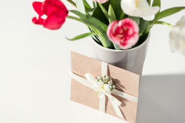 selective focus of beautiful blooming tulip flowers in vase and envelope on grey