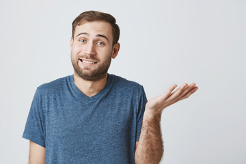 Studio shot of emotional clueless bearded male dressed in light blue t-shirt having confused...