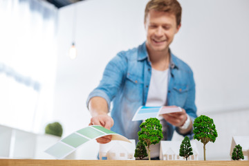 Suitable palette. Cheerful experienced skilled engineer feeling happy while being in his comfortable office and fining the most suitable color from a color palette