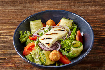 Fried Tofu Salad with Cucumbers, Tomatoes, Avocado and Sesame Seeds. Homemade asian vegetable and tofu salad in ceramic bowl on wooden background.