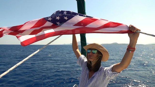 Portrait of happy woman with USA flag sailing boat on sea, slow motion shot at 240fps 
