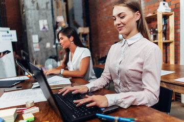 Friendly female office workers wearing formal workwear typing on laptop keyboard working in...