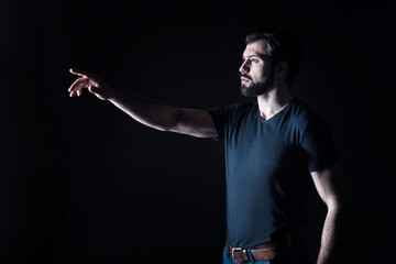 Over there. Nice pleasant handsome mans standing against black background and pointing with his hand while seeing something interesting