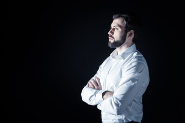 Obraz premium Handsome look. Serious nice bearded man standing cross handed and looking in front of him while being thoughtful