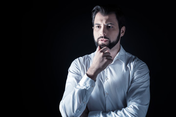 Pensive look. Smart nice handsome man standing against black background and thinking while looking for a solution