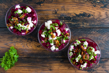 Vegetarian salad with baked beet, Greek yogurt, fresh parsley, walnuts and feta cheese in small glass bowls on the rustic wooden table, top view.