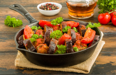 Black cast-iron skillet with Turkish kebab cooked with eggplant and tomatoes on rustic wooden table.