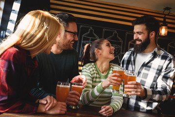 Smiling young people drinking craft beer in pub