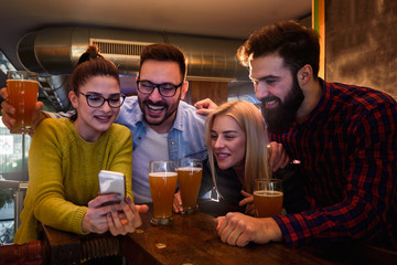 Friends in Pub drinking Beer and Looking at Smartphone