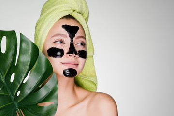 cute young girl with a green towel on her head, on her face a black mask against acne, day spa