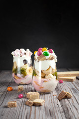 Dessert in a glass with a banana, cookies, candies, waffles and jelly on a wooden table