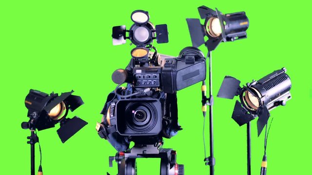 Bright spotlights stand near professional video camera on a green screen.