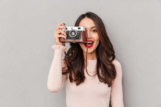 Image of pretty female photographer holding retro camera doing favorite shots isolated against gray background copy space
