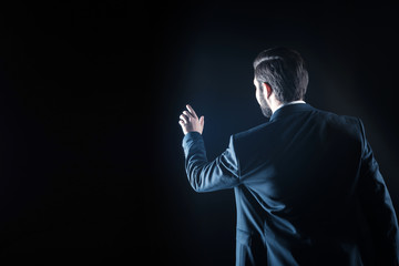 Professional tech. Nice smart handsome businessman standing against black background and touching the virtual screen while using modern technology