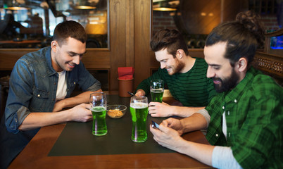 friends with smarphones and green beer at pub