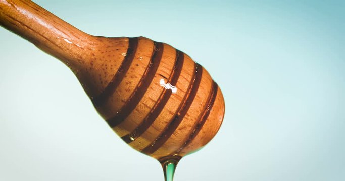 Close up pouring golden sweet honey dripping  on a honey dipper  vintage blue green  background , 4K Dci resolution