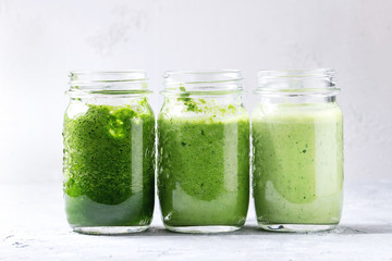 Variety of three color green spinach kale apple yogurt smoothie in mason jars in row over gray background. Healthy vegan detox eating.