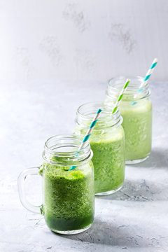 Variety of three color green spinach kale apple yogurt smoothie in mason jars with retro cocktail tubes over gray background. Healthy vegan detox eating.