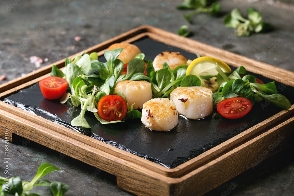 Wall mural fried scallops with lemon, cherry tomatoes and green salad served on wooden black slate serving boar