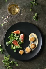 Foto op Aluminium Fried scallops with lemon, figs, sauce and green salad served on black plate with glass of white wine over old dark metal background. Top view, space. Plating, fine dining © Natasha Breen