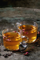 Two glasses of hot tea, rose buds, heart shaped tea strainer, pink sugar over old dark metal background. Space for text. Love Valentines day concept