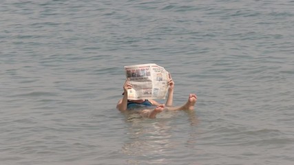 a woman reads a newspaper while floating in the dead sea on the israeli side