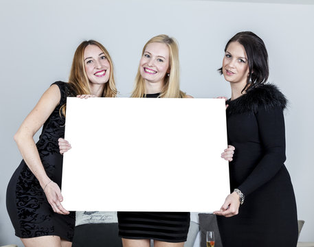 DREI FRAUEN IN KURZEN ELEGANTEN KLEIDERN HALTEN EINE WEISSE TAFEL IN DEN H&Auml;NDEN