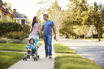 Couple Push Daughter In Stroller As They Walk Along Street