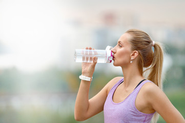 Profile portrait of sporty woman drinking in park after jogging