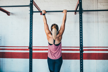Strong female athlete doing pull up in gym