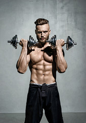 Fototapeta na wymiar Handsome man doing exercise with dumbbells. Photo of muscular man on grey background. Strength and motivation.