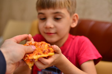 boy in red T-shirt eating pizza at home. portrait of a young man eating pizza, background