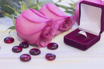 The concept of Love, Wedding, Proposal, Anniversary, St. Valentine's Day, Mother's Day with beautiful pink roses and a wedding ring in a red velvet box in a close up, light wooden background