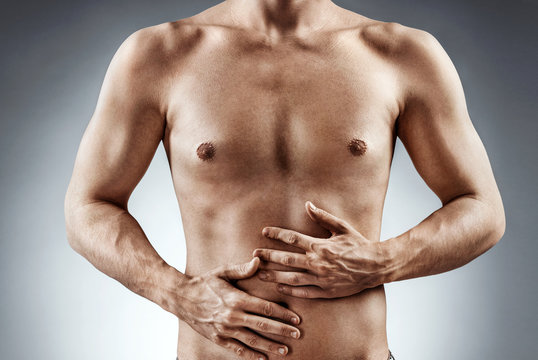 Man holding his stomach in pain. Photo of man with naked torso experience irritable bowel syndrome on grey background. Medical concept