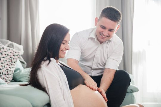Young pregnant couple relaxing at home, touching belly