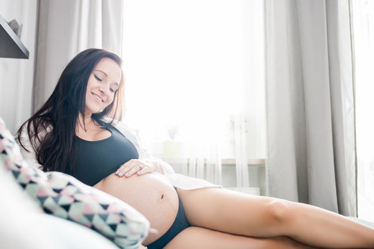 Relaxed smiling pregnant woman at home lying on sofa