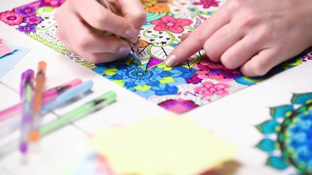 Colour video of a young unrecognisable woman colouring in an adult colouring book. New art therapy and stress management trend. Close up shot, hand detail.