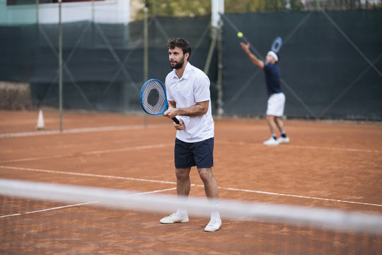 Group of friends play tennis a double match on a clay court