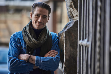 Portrait of smiling male leaning against wall while standing on street. He looking at camera....